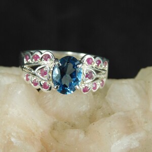 May include: A silver ring with a large blue gemstone surrounded by smaller pink gemstones.
