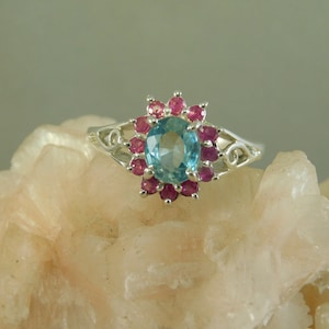 May include: A silver ring with a blue topaz gemstone surrounded by a halo of pink sapphires.