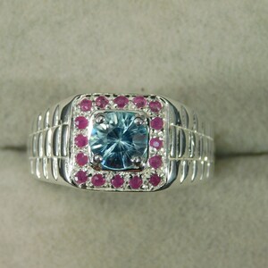 May include: A silver ring with a blue gemstone surrounded by pink gemstones.