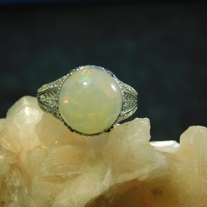 May include: A silver ring with a large, round, white opal gemstone set in a delicate, ornate design.