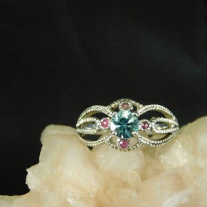 May include: A silver ring with a blue gemstone surrounded by five smaller pink gemstones.