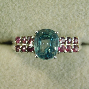 May include: A silver ring with a large oval blue gemstone surrounded by smaller pink gemstones.