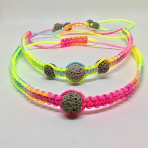 May include: Two colorful bracelets with lava rock beads. The bracelets are made with neon pink, yellow, blue, and green string.
