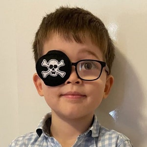 May include: A young child wearing glasses and a black eye patch with a white skull and crossbones design.