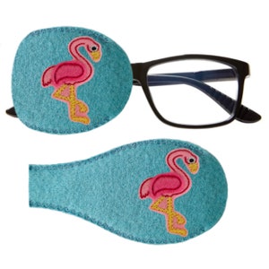 May include: Two blue felt eye patches with pink flamingo embroidery. The patches are designed to cover one eye at a time.