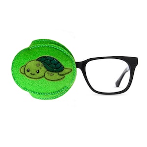 Peut inclure: Un cache-œil vert avec un motif de tortue de dessin animé mignon. Le cache-œil est fait de feutre doux et a une bordure noire cousue. Le cache-œil est attaché à une paire de lunettes noires.