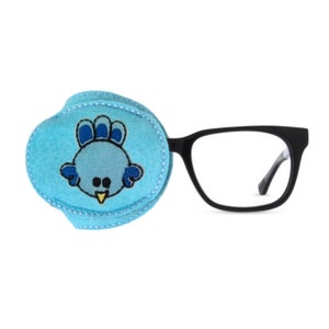 May include: A blue eye patch with an embroidered cartoon bird design. The eye patch is attached to a pair of black framed glasses.