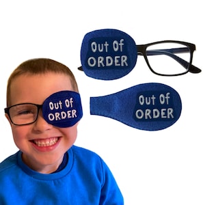 May include: A blue eye patch with the text "Out of Order" in white lettering. The eye patch is worn over a child's eye, who is also wearing glasses.