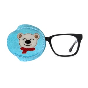 May include: A blue felt eye patch with a white polar bear wearing a red scarf embroidered on it. The eye patch is attached to a pair of black framed glasses.