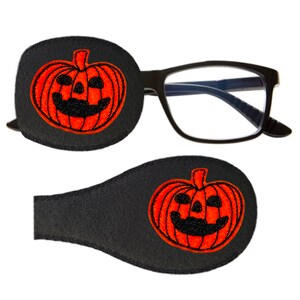May include: A pair of black eye patches with an orange pumpkin face embroidered on each patch. The patches are made of soft, black felt and are designed to cover one eye.
