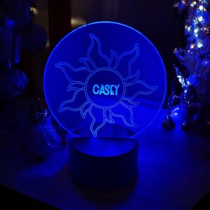 May include: A blue light-up nightlight with a clear acrylic base and a sun design with the name "CASEY" in the center.