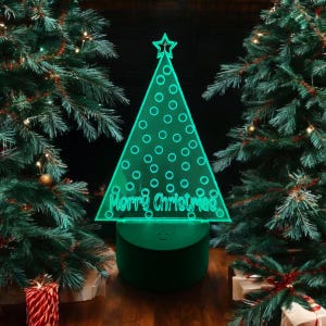 May include: A green light-up Christmas tree with a star on top and the words "Merry Christmas" inscribed on the front. The tree is sitting on a green base and is surrounded by Christmas trees.