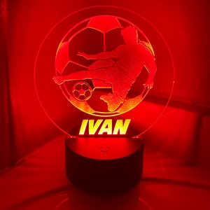 May include: A red LED night light with a silhouette of a soccer player kicking a ball. The name "IVAN" is written below the silhouette.
