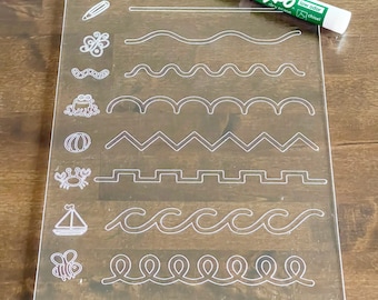 May include: A clear plastic dry-erase board with white lines and various images, including a butterfly, a worm, a frog, a pumpkin, a crab, a sailboat, and a bee. The board is designed for tracing and practicing fine motor skills. The board is accompanied by a green dry-erase marker with the text "Expo low odor dry erase chisel" on the side.