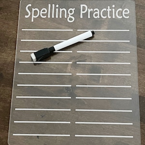 May include: A clear acrylic dry-erase board with white lines and the text "Spelling Practice". A white dry-erase marker is lying on the board.