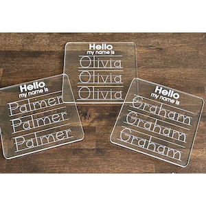 May include: Three clear acrylic practice boards with dotted lines for tracing letters. The boards have the text "Hello my name is" and the names "Olivia", "Palmer", and "Graham" written on them.