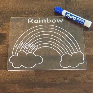 May include: A clear acrylic dry-erase board with a rainbow and clouds design. The board has the word "Rainbow" printed at the top and the colors of the rainbow listed on the left side. An Expo low odor dry-erase marker is also pictured.
