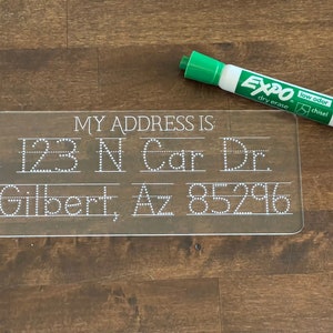 May include: A clear plastic dry-erase board with white dotted lines and the text "MY ADDRESS IS:"  The board is used for practicing writing an address. The address is "123 N Car Dr. Gilbert, Az 85296". A green dry-erase marker is next to the board.