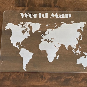 May include: A white world map etched onto a clear acrylic surface. The map is outlined in white and includes all the continents. The words "World Map" are printed in white at the top of the surface.