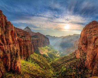 Puede incluir: Una vista panorámica de un cañón con acantilados de roca roja y un valle verde y exuberante. El sol brilla intensamente en el cielo azul, proyectando largas sombras sobre el paisaje.
