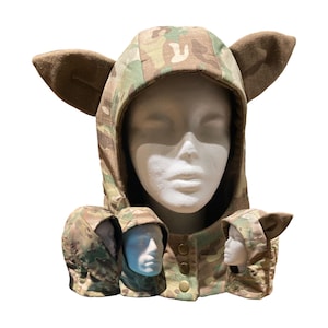 Puede incluir: Una capucha con estampado de camuflaje con orejas grandes y puntiagudas de color marrón. La capucha está abotonada en el cuello y se muestra en una cabeza de maniquí. También se muestran capuchas más pequeñas con orejas.