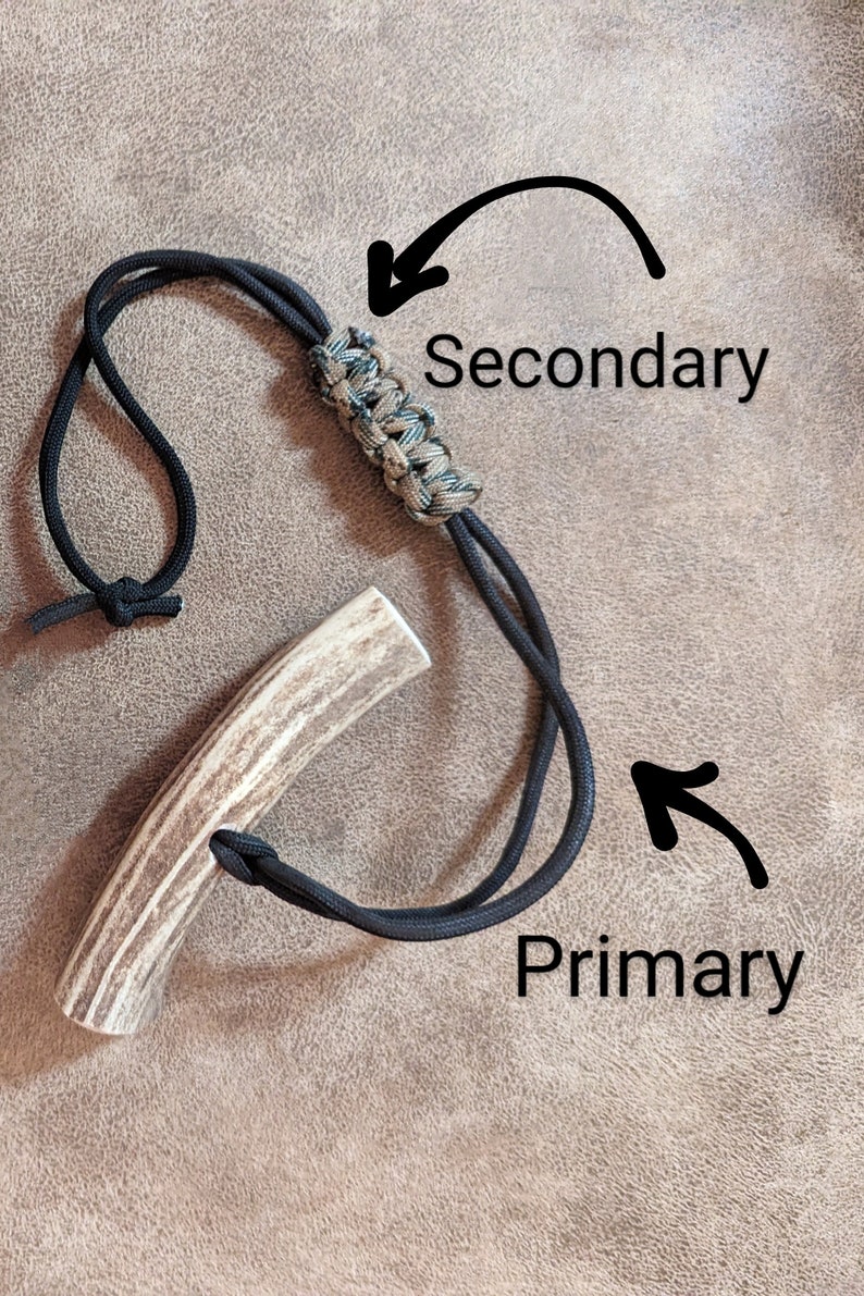 K&ouml;nnte beinhalten: Ein handgefertigter Geweihgriff mit einem schwarzen Kordelband. Die Kordel ist um das Geweih geknotet und hat einen geflochtenen Abschnitt mit gr&uuml;nen und beigen Akzenten. Die W&ouml;rter "Primary" und "Secondary" sind auf dem Bild geschrieben.