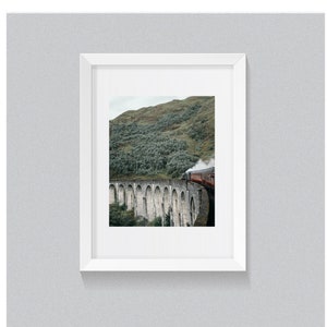 May include: Framed print featuring a red steam train crossing a stone viaduct. The bridge arches over a valley with a green, tree-covered hillside in the background. The print is in a white frame.