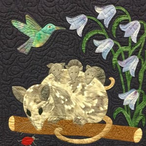 May include: A gray and white opossum with four babies on its back sits on a brown branch. A hummingbird with green and blue feathers flies above the opossum. The background is a dark blue fabric with a quilted pattern. There are several blue bell flowers with green stems and leaves.