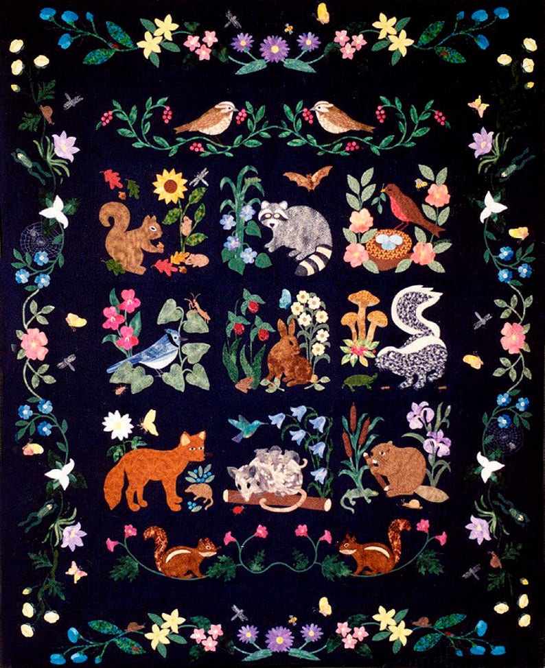 May include: A colorful quilt with a dark blue background featuring various animals and plants. The animals include a fox, a raccoon, a squirrel, a beaver, a rabbit, a skunk, a bird, and a hedgehog. The plants include flowers, leaves, and mushrooms.