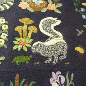 Puede incluir: Una tela acolchada azul con una variedad de dise&ntilde;os aplicados, incluyendo una mofeta, champi&ntilde;ones, una tortuga y flores. La tela es de color azul oscuro y los dise&ntilde;os est&aacute;n en varios tonos de marr&oacute;n, verde, blanco y negro.