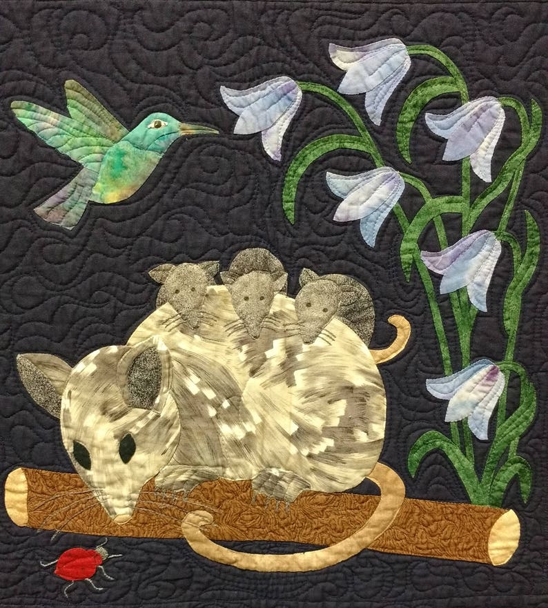 May include: A gray and white possum with three babies on its back sits on a brown branch. A hummingbird with green and blue feathers flies above the possum. The background is a dark blue fabric with blue and white flowers.
