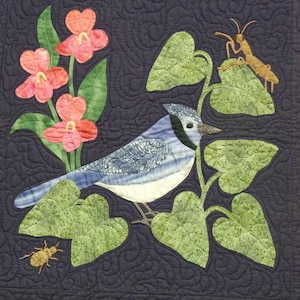 May include: A blue jay perched on a green leafy vine with pink flowers and two brown insects. The background is a dark blue fabric.