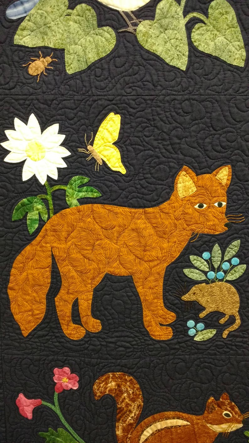 Puede incluir: Una tela acolchada azul oscuro con un zorro bordado, una mariposa, una flor, un escarabajo, una ardilla y un rat&oacute;n. La tela est&aacute; decorada con un patr&oacute;n de enredadera de hojas.