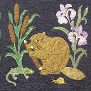 May include: A detailed quilt featuring a beaver holding a branch, surrounded by cattails, irises, and bluebell flowers. A lizard and snail are also depicted. The quilt has a dark blue background with quilted wavy lines.
