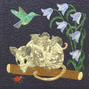 May include: A quilted wall hanging featuring a gray opossum with four babies on its back, perched on a brown branch. A hummingbird hovers above, and a red ladybug crawls on the branch. The background is a dark blue fabric with a swirling pattern.