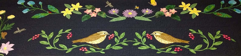 May include: A black fabric with embroidered yellow flowers, green leaves, and two brown birds on a vine with red berries.