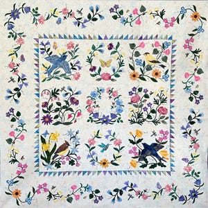 May include: A floral quilt with a white background, featuring nine square panels with birds, butterflies, and flowers. The border has a repeating floral pattern with butterflies and dragonflies. The quilt is decorated with a variety of colors, including pink, blue, yellow, and purple.