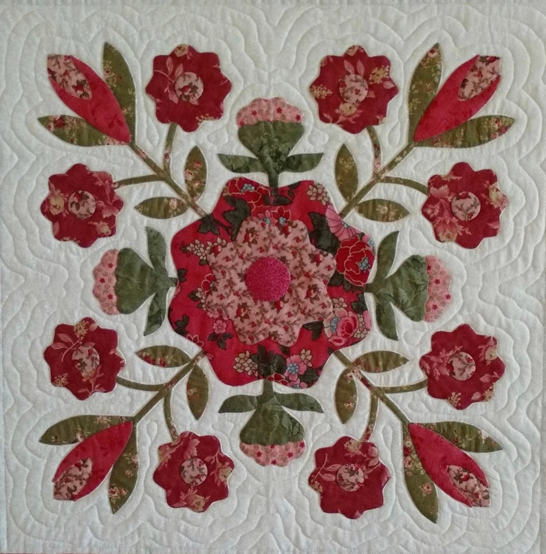 May include: A quilt block with a floral design featuring red, pink, and green flowers. The flowers are arranged in a symmetrical pattern on a white background.