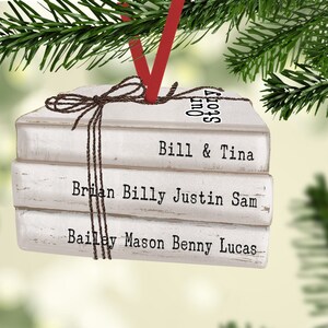 May include: A white book-shaped Christmas ornament with the text "Our Story" on the top book, "Bill & Tina" on the middle book, and "Brian Billy Justin Sam" and "Bailey Mason Benny Lucas" on the bottom two books.