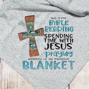 以下が含まれることがあります： グレーのフリースブランケットに、ターコイズブルーの十字架と「This is my Bible Reading Spending Time With Jesus Praying Wrapped in His Presence Blanket」というテキストが書かれています。