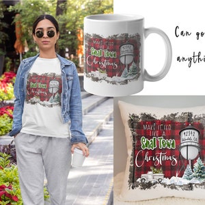 Könnte beinhalten: Weißes T-Shirt, Tasse und Kissen mit Weihnachtsdesign. Das Design umfasst ein rot-schwarzes Karomuster, einen Wasserturm, einen LKW mit Weihnachtsbaum und den Text "Make it feel like a Small Town Christmas."