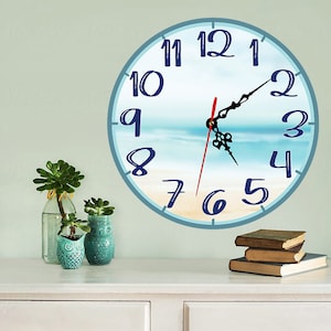 Könnte beinhalten: Eine blaue und weiße Uhr im Strandthema mit einem roten Stundenzeiger und einem schwarzen Minutenzeiger. Die Uhr steht auf einer weißen Kommode mit drei darauf gestapelten Büchern.