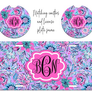 May include: A set of three matching personalized items featuring a floral design in shades of pink, blue, and green. The set includes two round coasters and a license plate frame. Each item features a monogram in a pink circle with a white outline.