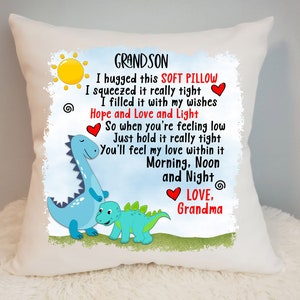 May include: White pillow featuring a blue dinosaur and a smaller green dinosaur. The pillow has a message that reads "Grandson I hugged this soft pillow I squeezed it really tight I filled it with my wishes Hope and Love and Light So when you're feeling low Just hold it really tight You'll feel my love within it Morning, Noon and Night Love, Grandma".