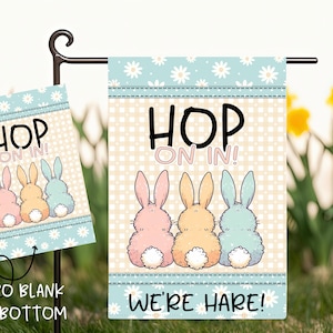 May include: A garden flag and a smaller sign with the text "HOP ON IN!" and "WE'RE HARE!" featuring illustrations of pastel-colored bunnies. The signs have a light blue floral border and a checkered background.