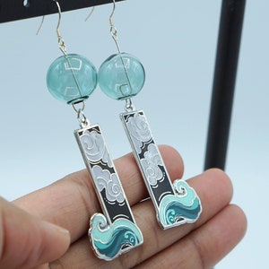May include: A pair of silver dangle earrings with a teal and white cloud design and a teal glass bead at the top.