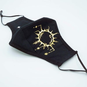 May include: Black face mask with a gold sun and moon design. The mask has adjustable ear loops.
