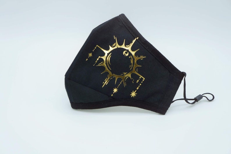 May include: Black face mask with a gold sun and stars design.