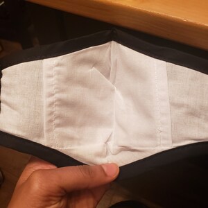 May include: A black fabric face mask with a white cotton lining. The mask is folded in half, showing the inside lining.