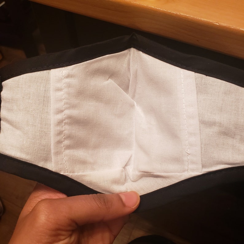 May include: A black fabric face mask with a white cotton lining. The mask is folded in half, showing the inside lining.